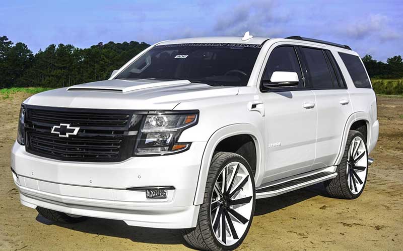 The front and drivers side of a white Tahoe Premier Edition in a mud field
